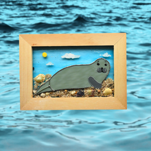 Load image into Gallery viewer, Framed glass artwork of a seal on a beach with ocean waves in the background