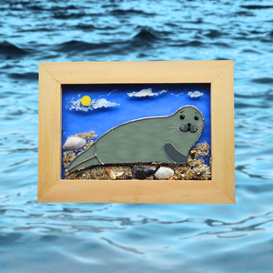 Framed glass artwork of a seal on a beach with ocean waves in the background